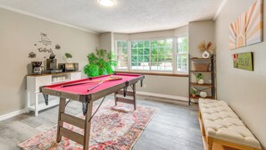Une table de billard dans une pièce avec une fenêtre, un banc et une étagère ornée d’objets décoratifs.