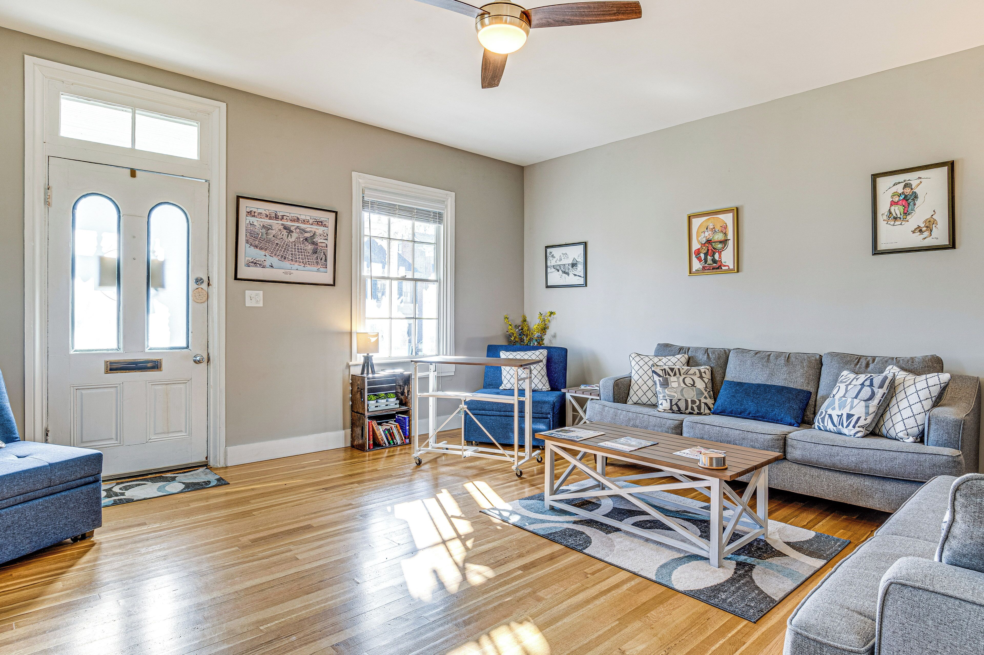 A living room with a grey sofa, a blue armchair, a wooden coffee table, and a ceiling fan.