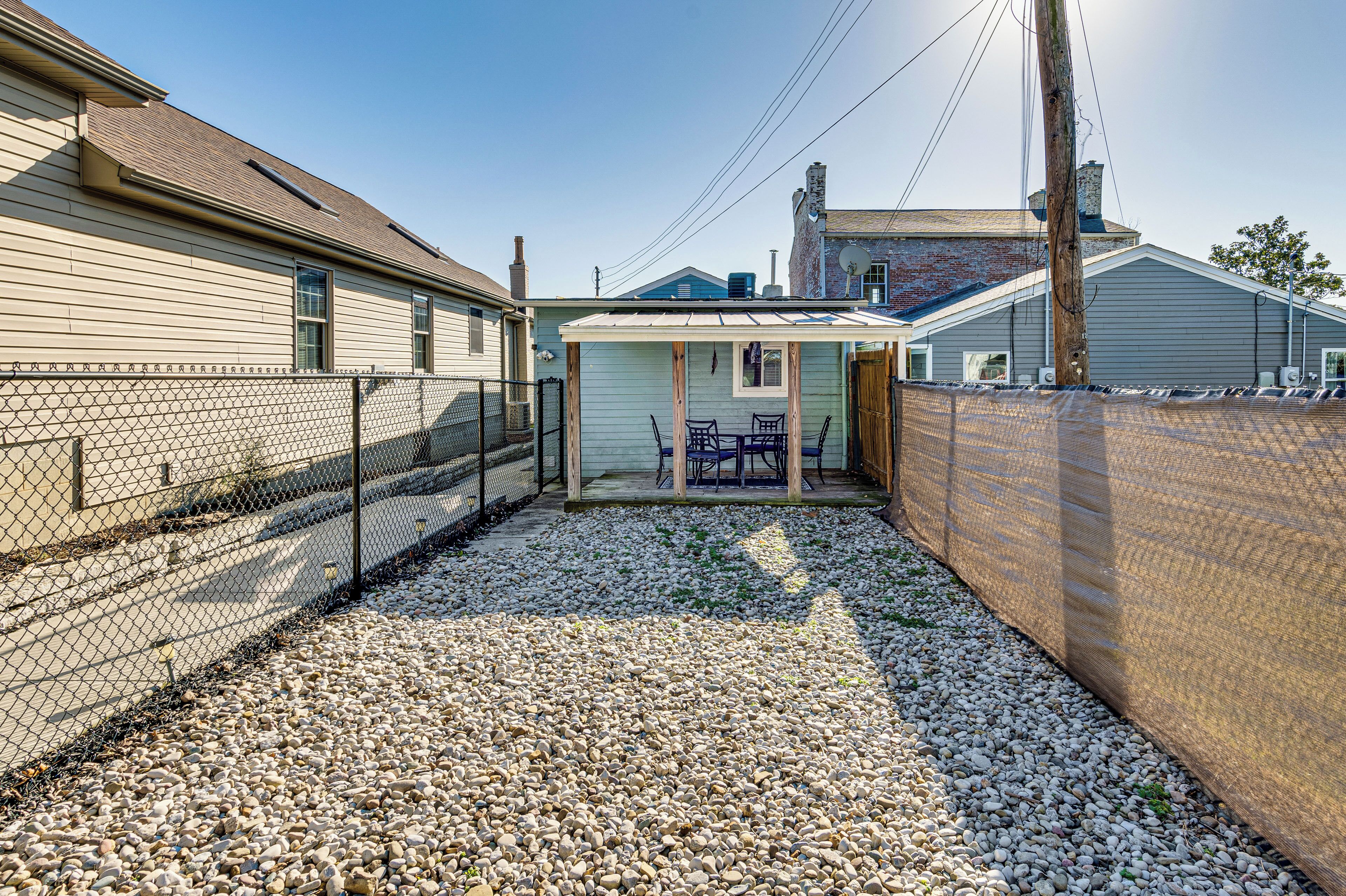 A fenced backyard with a gravel path leading to a covered patio area with outdoor furniture.