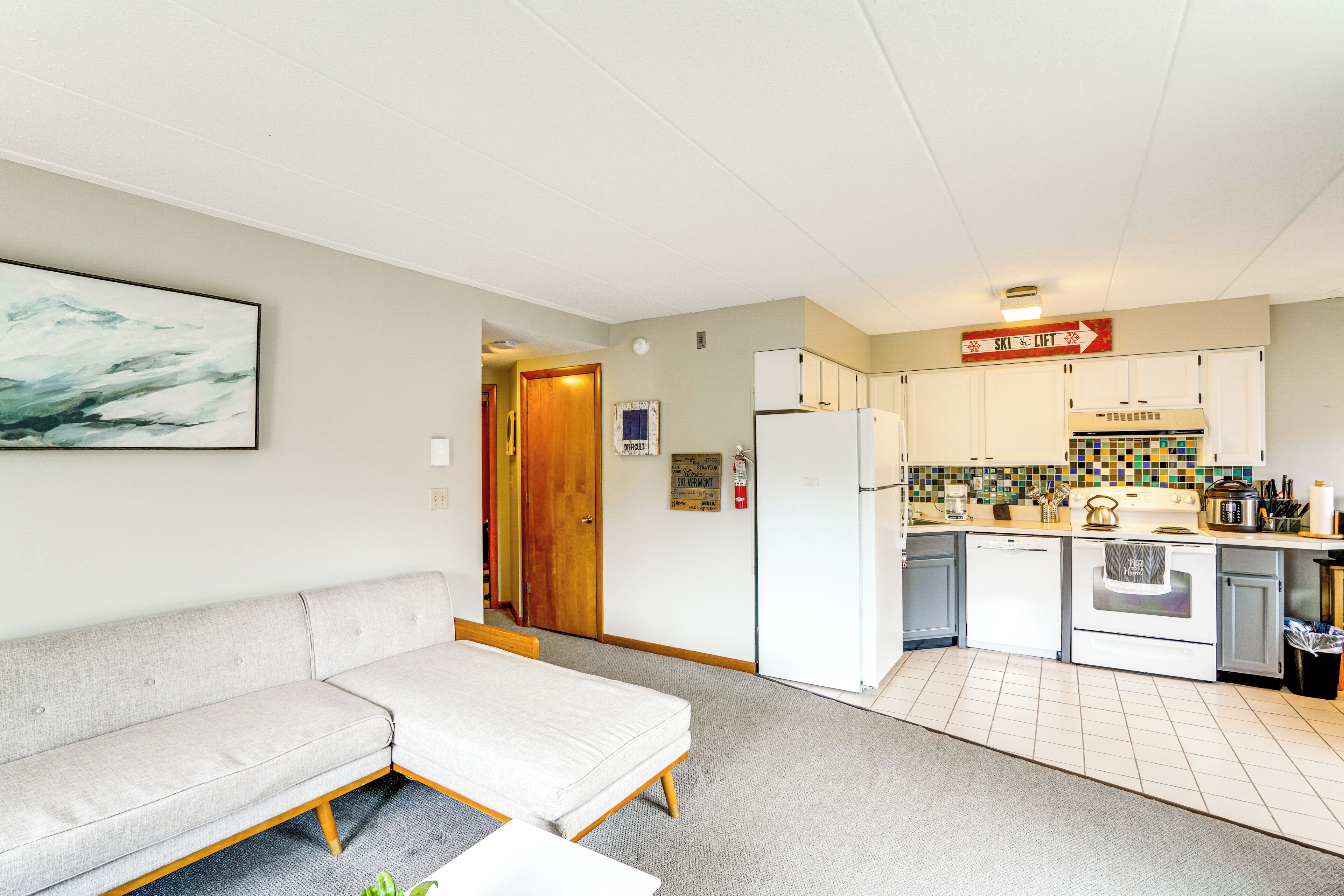 A compact living space with a sofa, kitchenette, and a door leading to another room.