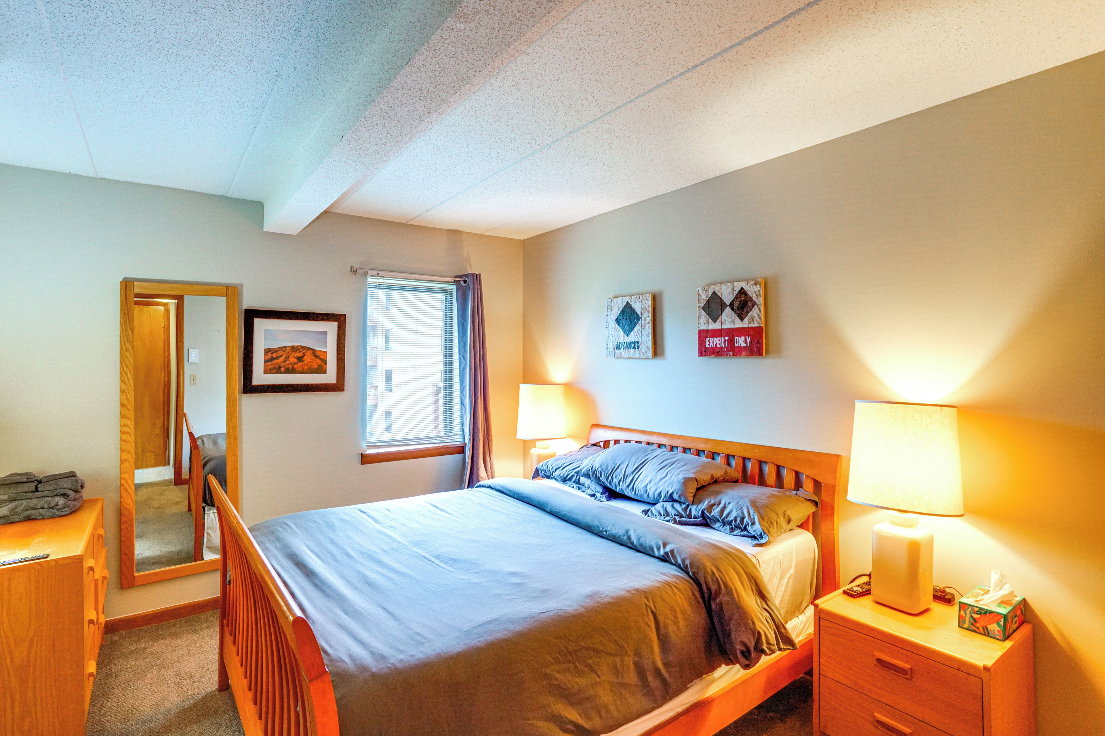 A bedroom with a bed, bedside tables, a mirror, a window, and wall decorations.