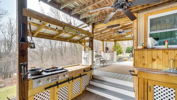 Una cocina campestre de madera con una parrilla, un comedor con sillas y vistas a los árboles circundantes.