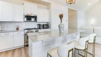 A modern kitchen with white cabinetry, a central island with bar stools, stainless steel appliances, and a decorative vase.