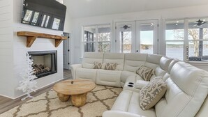 A modern living room with a sectional sofa, a fireplace, and large windows offering a view of a lake.