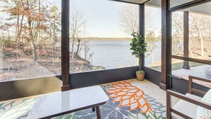 A room with large windows, a view of a lake, a potted plant, and a patterned rug.