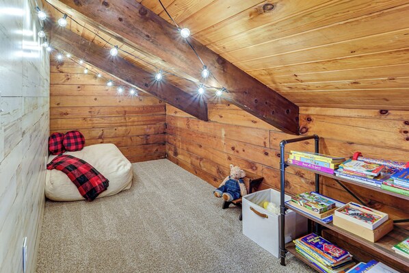 A cozy attic bedroom with a sloped ceiling, a wooden bunk bed, a small desk with books, and string lights. - Family-friendly Tyrone Cabin w/ Deck Near Hiking (Tyrone)