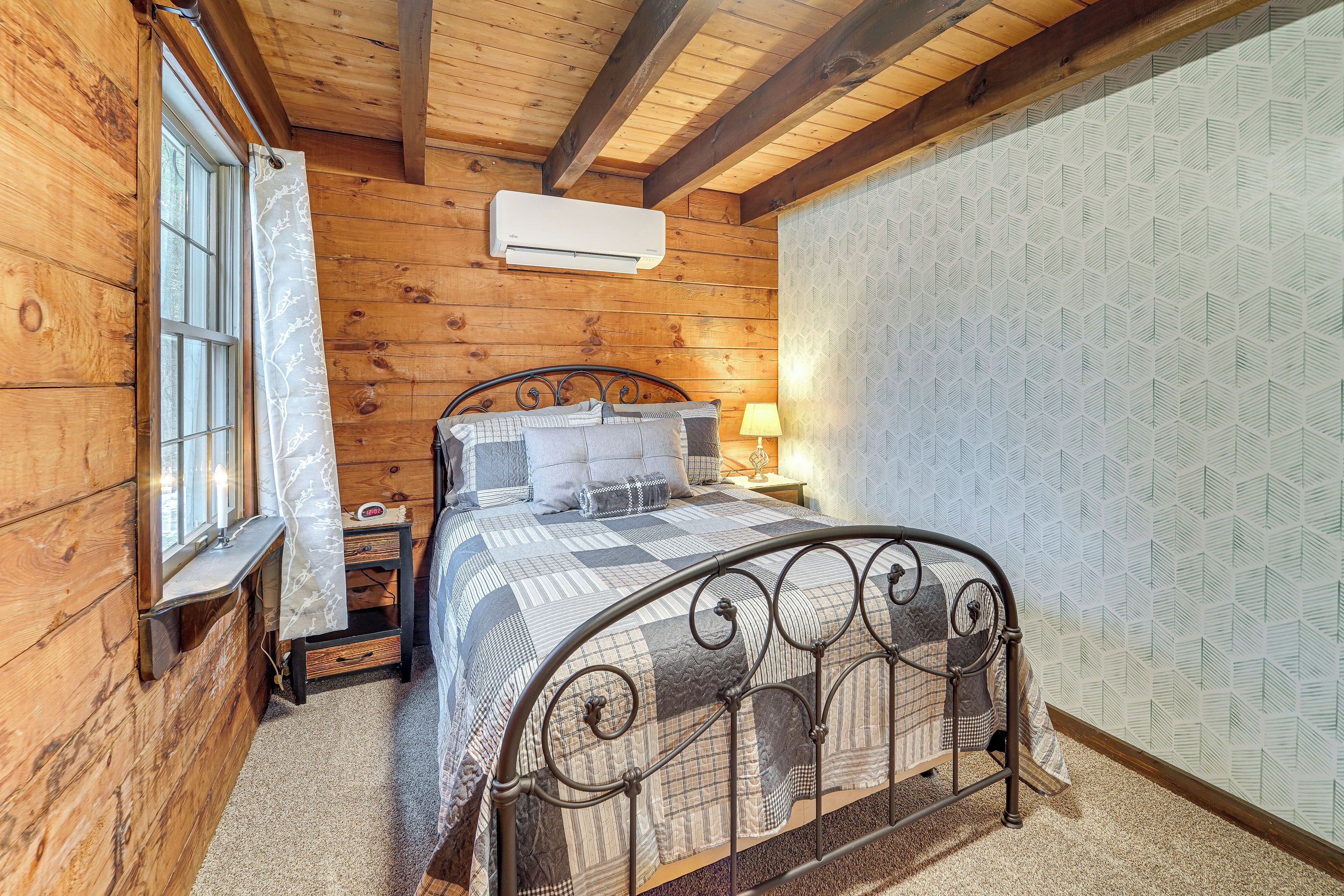 Dormitorio de cabaña de madera con cama, mesita de noche y ventana con cortinas.
