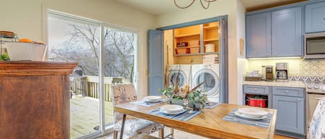 A kitchen with a dining table, chairs, a chandelier, and a view through the glass door.
