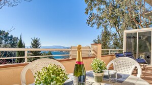 A table set with a bottle of champagne, glasses, and potted plants on a balcony overlooking a scenic view. - Apartment in Roses With Waterfront Views (Roses)