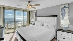 A bedroom with a large bed, a ceiling fan, a nightstand with a lamp, and a view of the ocean through a sliding door. - Seaside Beach & Racquet 5817 by Liquid Life (Orange Beach)
