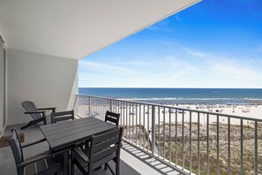 A balcony with a table and chairs, overlooking a beach with people and umbrellas.