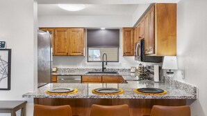 Una cocina moderna con armarios de madera, un refrigerador de acero inoxidable, un microondas integrado y una encimera de granito.
