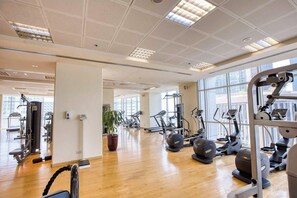 Une salle de sport spacieuse, dotée de divers appareils d’exercice, de grandes fenêtres et d’un plancher en bois.