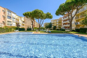A swimming pool surrounded by multi-story buildings with balconies, trees, and a clear sky. - Beachside Stay w/ Pools (Castello d'Empuries)