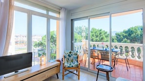 A balcony with a TV, a chair, a table, and a sofa. - Beachside Stay w/ Pools (Castello d'Empuries)