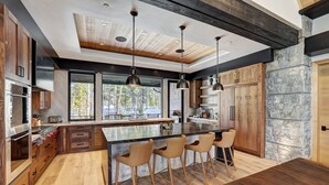 A modern kitchen with a large island, bar stools, and a stone accent wall.