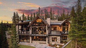 A modern log cabin with a large deck, stone exterior, and a hot tub in the backyard.