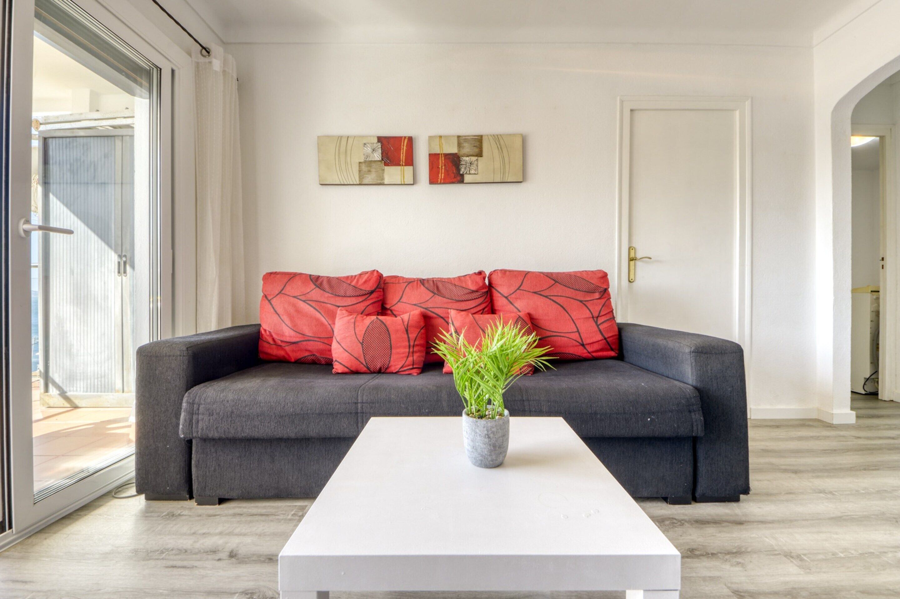 A modern living room with a grey sofa, red cushions, a white coffee table, and two abstract wall art pieces.