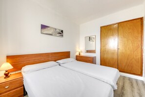 A hotel room with a double bed, a nightstand with a lamp, a wooden wardrobe, and a painting on the wall. - Apartment in Rosas Near Playa de Canyelles (Roses)