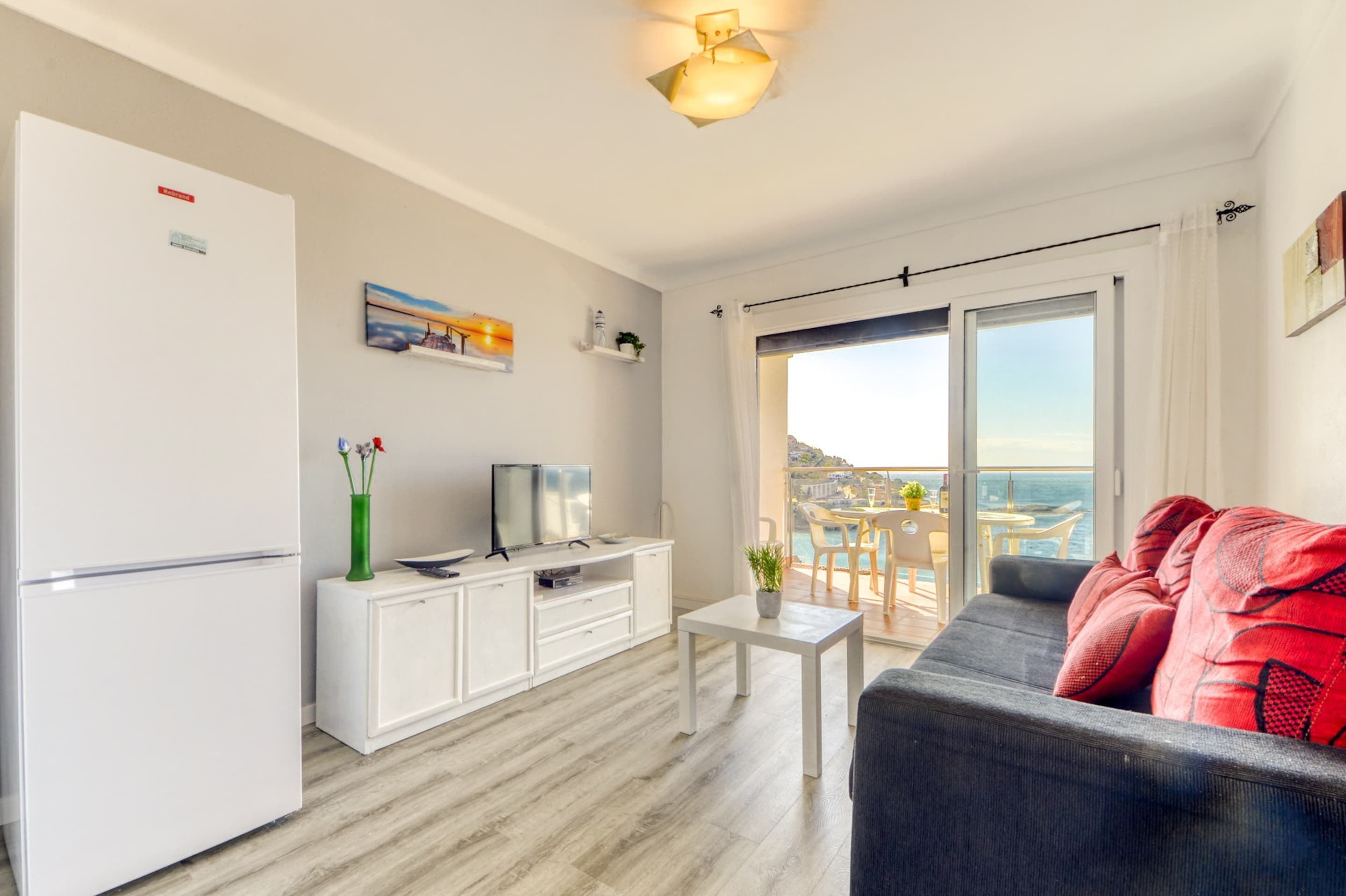 En moderne stue med sofa, fjernsyn, et lille bord og en balkon med udsigt.