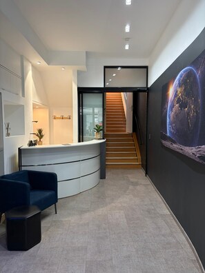 A modern reception area with a curved desk, a staircase, and a large wall mural. - Spacehotel-Karlsruhe  (Karlsruhe)