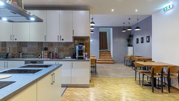 A modern kitchen with a central island, wooden flooring, and a dining area with tables and chairs. - Spacehotel-Karlsruhe  (Karlsruhe)