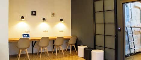 Una habitación con piso de madera, un escritorio con computadora, cuatro sillas y un ventanal con vistas a una estructura blanca en el exterior.