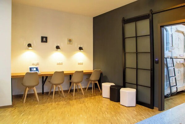 A room with a wooden floor, a desk with a computer, four chairs, and a sliding door with a view of a white structure outside. - Spacehotel-Karlsruhe  (Karlsruhe)