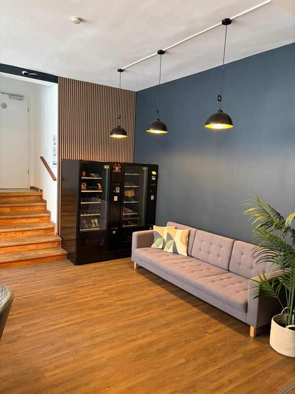 Un interior moderno con un sofá gris, suelo de madera, una escalera y una máquina expendedora.