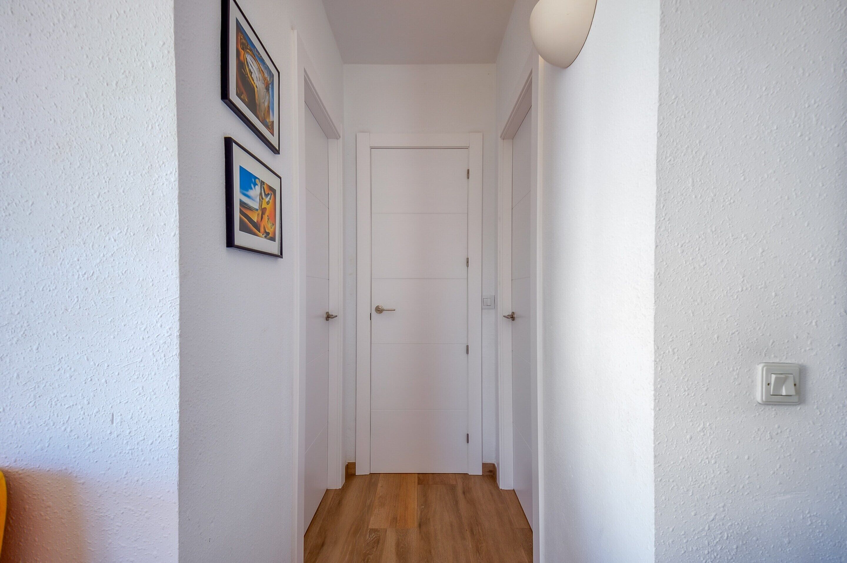 A narrow hallway with white walls, a wooden floor, and a white door at the end.