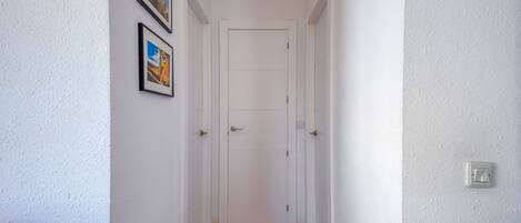 A narrow hallway with white walls, a wooden floor, and a white door at the end.