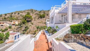 A hillside residential area with white buildings, a paved pathway, and rocky terrain. - Apartment in Roses Near Canyelles Beach (Roses)