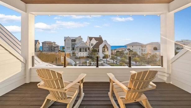 A balcony with two wooden chairs facing a view of houses and the ocean. - 1 HOUSE OFF THE BEACH! Private Pool, LSV/Golf Cart, Bikes, Games, Gym! Sleeps 22! (Santa Rosa Beach)