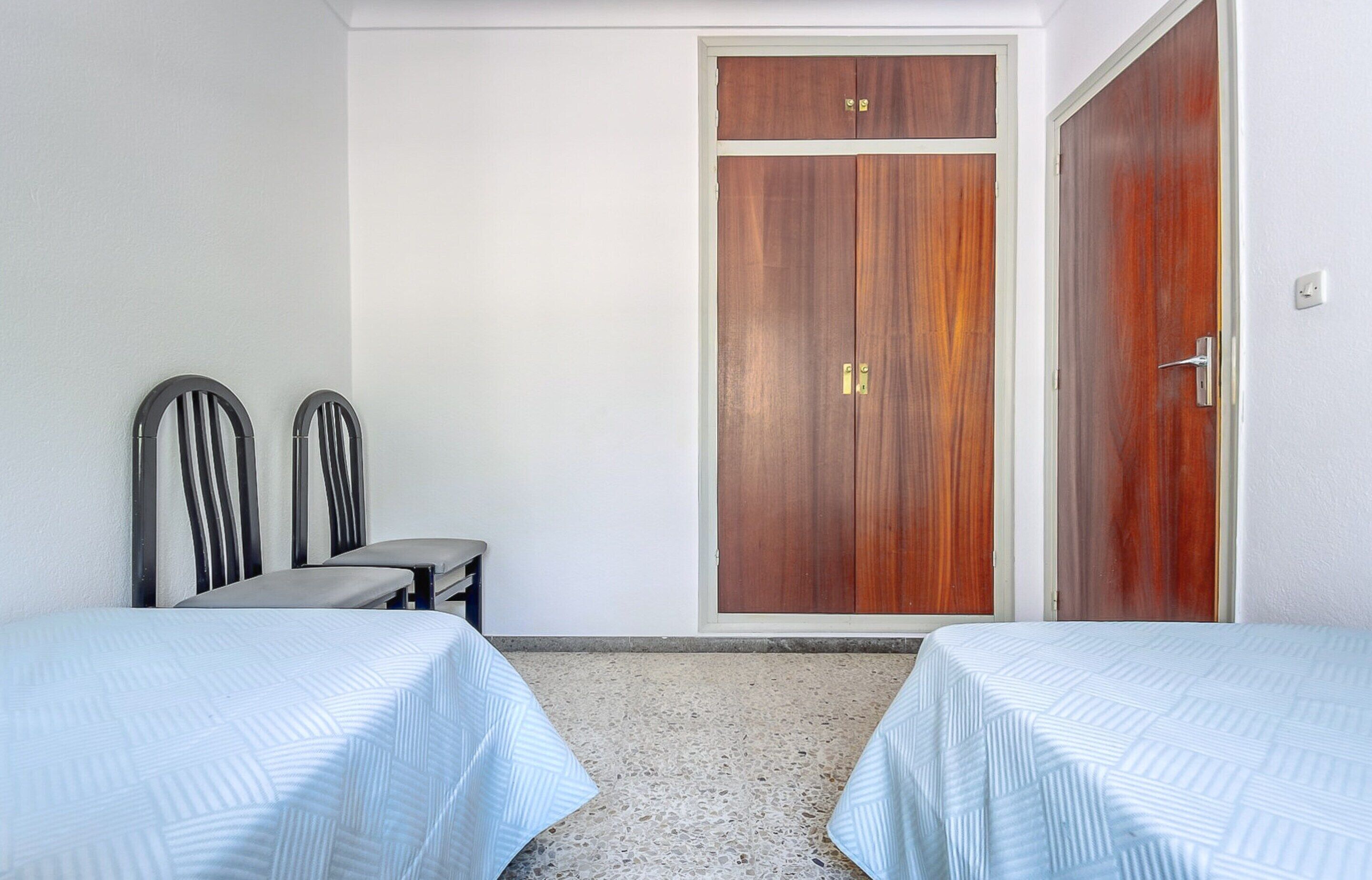 Une chambre avec deux lits, une armoire en bois et une petite table avec des chaises.