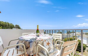 A round table with a nautical-themed tablecloth, a bottle of champagne, and glasses, set on a balcony with a view of the sea and buildings. - Apartment With Scenic View (Roses)