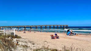 A beach with a pier extending into the ocean, sandy beach, and people relaxing.