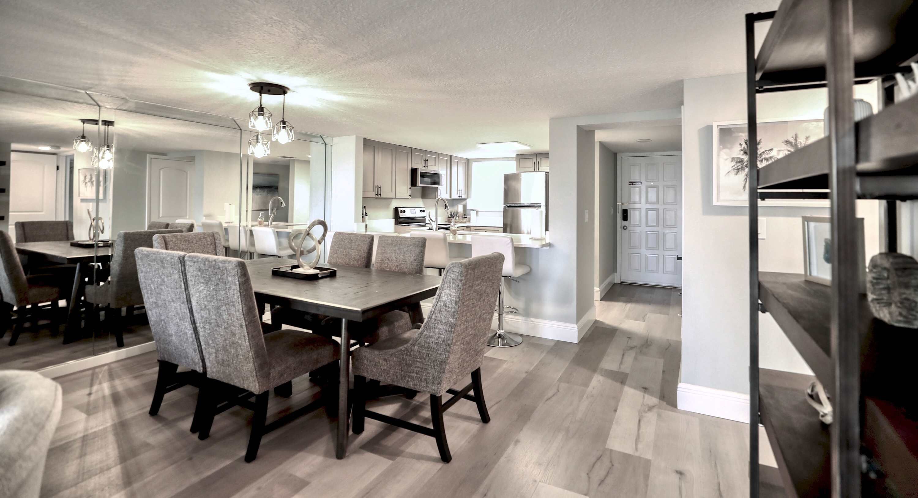 A modern kitchen with stainless steel appliances, a dining area with a large table and chairs, and a hallway leading to a bedroom.