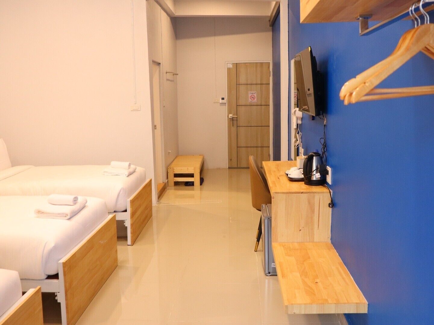 A hotel room with two beds, a small wooden table, a desk with a chair, a television mounted on the wall, and a blue accent wall.