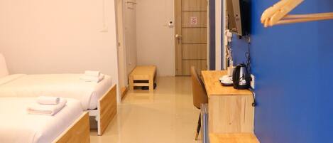 A hotel room with two beds, a small wooden table, a desk with a chair, a television mounted on the wall, and a blue accent wall.