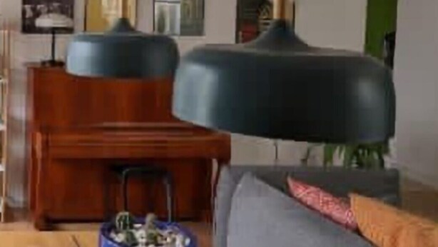 Una sala de estar moderna con una mesa de centro de madera, una mesita auxiliar azul y un sofá gris con un cojín rojo. Hay dos lámparas colgantes en el techo.