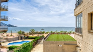 Vista de una piscina, un césped cuidado y una playa con un barco a lo lejos.