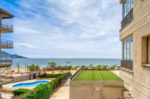 A view of a swimming pool, a well-maintained lawn, and a beach with a boat in the distance. - Apartment in Roses Near Platja del Eastrell (Roses)