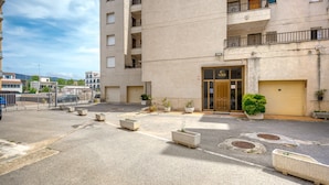 Un edificio de varios pisos con fachada color beige, entrada protegida por una reja y macetas con plantas.