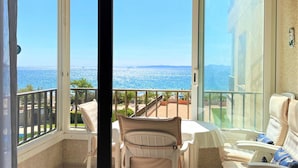 Un balcón con vista al mar, una mesa con sillas y una puerta de vidrio.