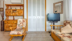 Una sala de estar con un aparador de madera, un sillón mecedora, un sofá, un televisor y un armario con puertas batientes.