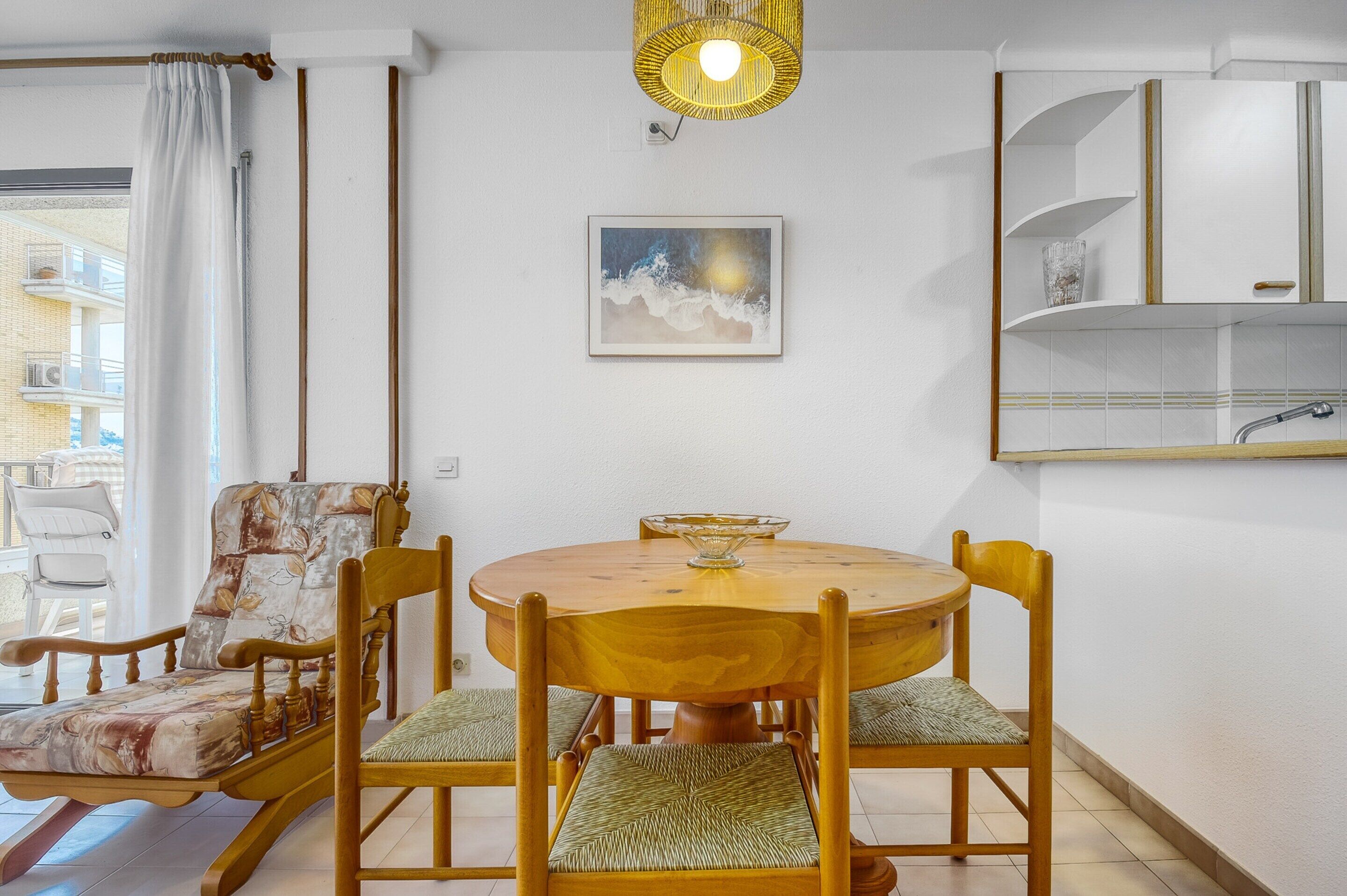 A dining area with a round wooden table, four chairs, and a hanging light fixture.