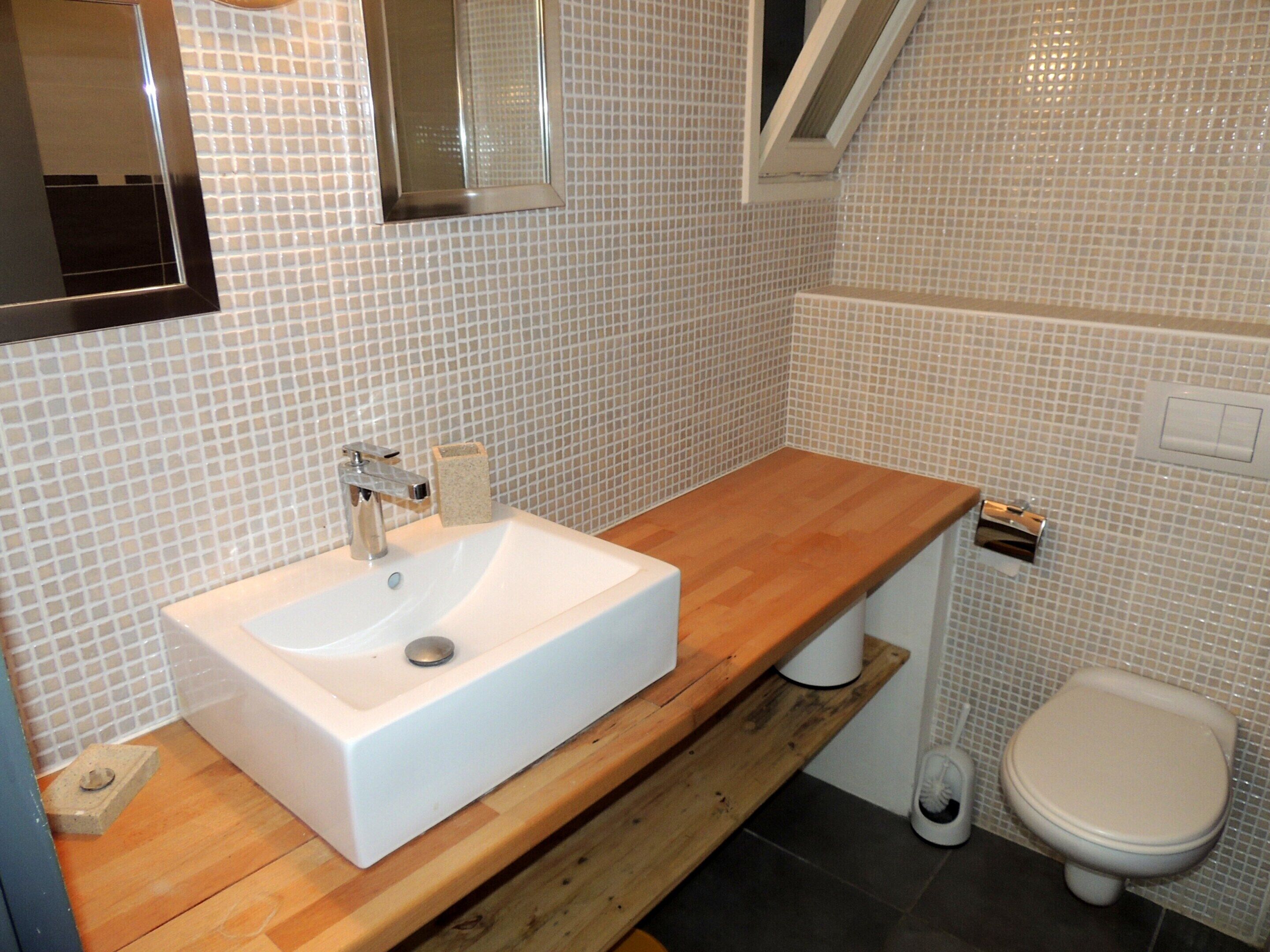 A bathroom with a white sink, wooden countertop, and a white toilet.