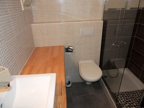 A bathroom with a wooden vanity, a toilet, and a shower area. - Apartment in Roses With Balcony (Roses)