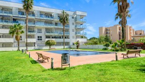 A modern apartment building with balconies, a swimming pool, and a grassy courtyard with benches. - Charming Apartment With Patio (Roses)