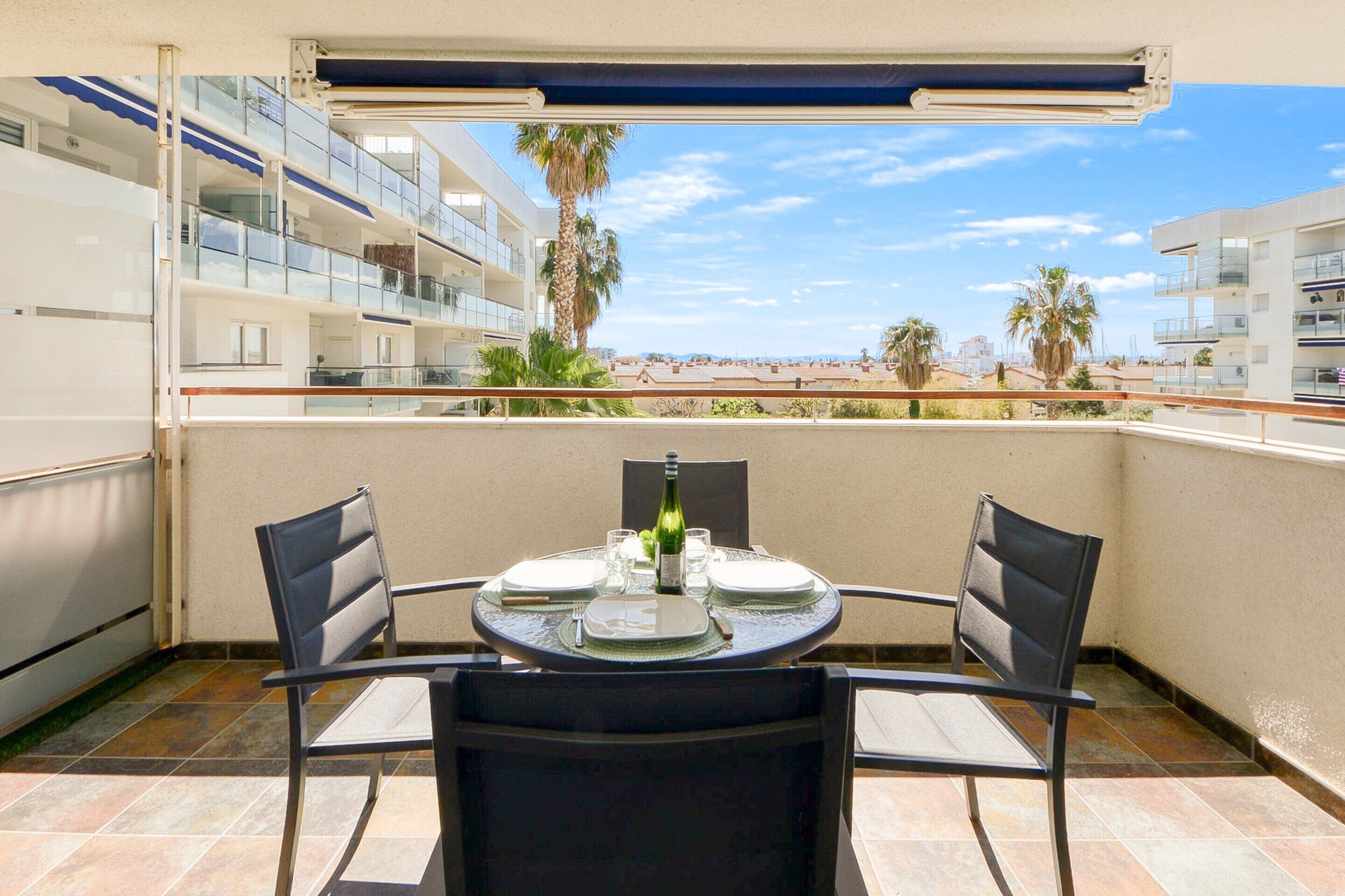 A balcony with a round table set for two, overlooking a beach and palm trees.